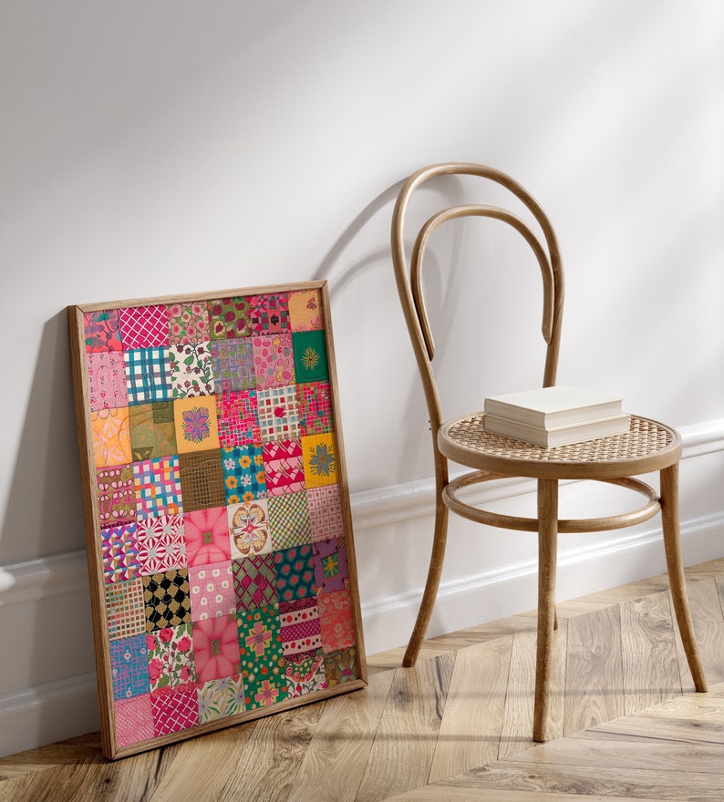 May include: A framed print of a colorful patchwork quilt with various patterns and colors, including pink, red, green, yellow, and blue. The print is hanging on a white wall next to a wooden chair.