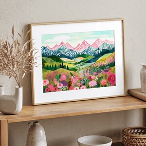 May include: A framed watercolor painting of a mountain range with pink peaks and a valley filled with colorful wildflowers. The mountains are in the background and the wildflowers are in the foreground. The painting is set against a white background.