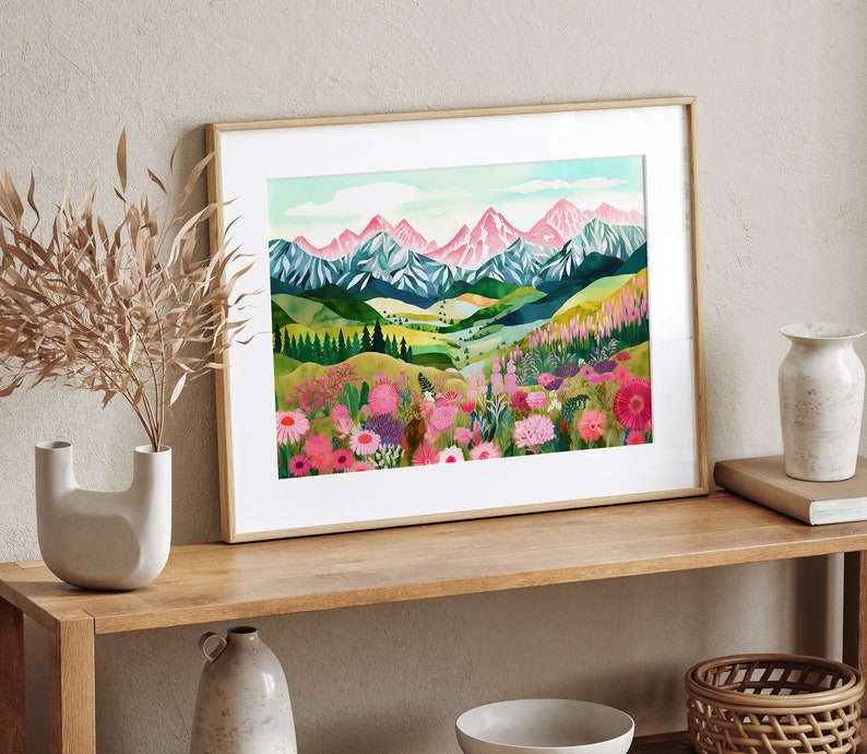 May include: A framed watercolor painting of a mountain range with pink peaks and a valley filled with colorful wildflowers. The mountains are in the background and the wildflowers are in the foreground. The painting is set against a white background.