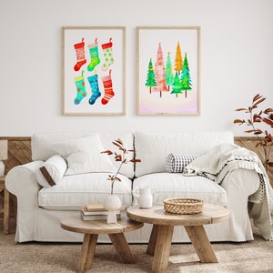 Puede incluir: Dos pinturas de acuarela enmarcadas en una pared blanca sobre un sof&aacute; blanco con dos mesas de caf&eacute; de madera. La pintura de la izquierda presenta seis calcetines de Navidad coloridos. La pintura de la derecha presenta un grupo de cinco &aacute;rboles de Navidad coloridos.
