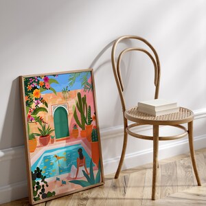 May include: A framed illustration of a woman sitting by a pool in a courtyard with a green door, cacti, and flowers. The pool is blue and the woman is wearing a white dress. The illustration is in a colorful style.