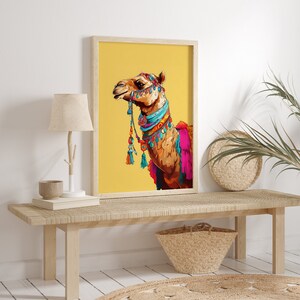 May include: A framed print of a camel with colorful decorations on a yellow background. The camel is facing to the right and has a blue and turquoise collar with tassels.