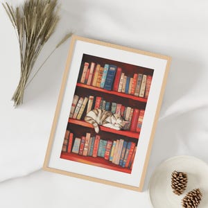 May include: A framed illustration of a cat sleeping on a bookshelf filled with colorful books. The cat is white and gray with black stripes. The books are mostly red and have gold lettering.