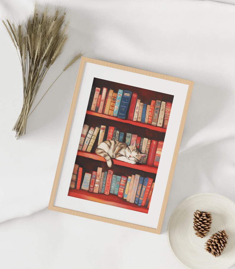 May include: A framed illustration of a cat sleeping on a bookshelf filled with colorful books. The cat is white and gray with black stripes. The books are mostly red and have gold lettering.