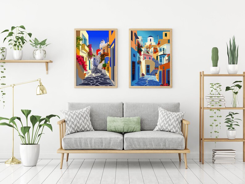 May include: Two framed illustrations of colorful buildings in a Greek village. The illustrations are set against a white wall with a couch and plants in the foreground.