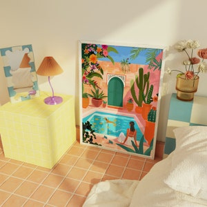 May include: A colorful illustration of a Moroccan courtyard with a swimming pool, potted plants, and a woman sitting by the water. The artwork is framed in a white frame.