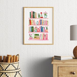 May include: Watercolor painting of a pink bookshelf with books, plants, and vases. The bookshelf has four shelves and is filled with various colored books. There are small plants and flowers in pots on each shelf. The painting is framed in a light wood frame.