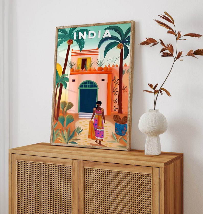 May include: A colorful illustration of a building in India with a woman in a pink and orange sari standing in front of it. The building has a green door and a red roof. The illustration is framed in a wooden frame.