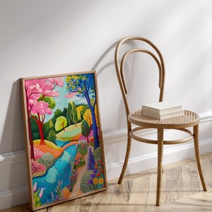 May include: A framed art print depicts a colorful landscape with a river, trees, and flowers. The artwork features vibrant hues of pink, blue, green, and yellow. A wooden chair with a woven seat and a stack of books sits nearby.