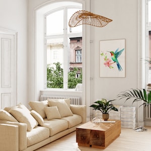 Puede incluir: Un sof&aacute; beige claro con varios cojines en una sala de estar con una mesa de caf&eacute; de madera, una ventana grande y una impresi&oacute;n enmarcada de un colibr&iacute; con flores rosas.
