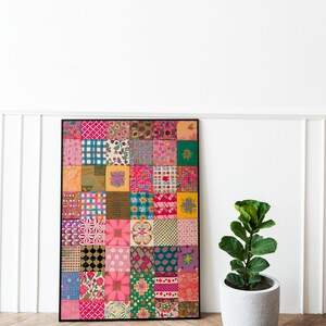 May include: A framed artwork featuring a colorful patchwork quilt design with various patterns and colors, including pink, green, yellow, and blue. The artwork is displayed on a wooden floor with a potted plant in the foreground.