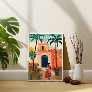 May include: A framed illustration of a colorful building with a woman in a pink and blue dress walking towards the entrance. The building is surrounded by palm trees and the text "INDIA" is at the top of the image.