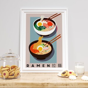 Pode incluir: Um p&ocirc;ster emoldurado branco com fundo azul que apresenta duas tigelas de macarr&atilde;o ramen. As tigelas est&atilde;o cheias de macarr&atilde;o, caldo e v&aacute;rios acompanhamentos, incluindo um ovo cozido, algas e carne. O p&ocirc;ster tem o texto "RAMEN 拉麺" na parte inferior.
