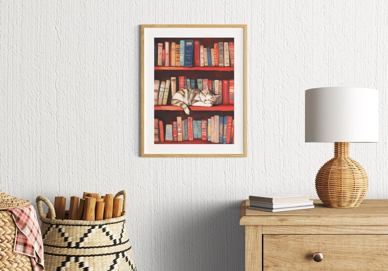 May include: A framed illustration of a cat sleeping on a bookshelf filled with colorful books. The cat is curled up on the top shelf, with its head resting on a book. The bookshelf is made of wood and has a red background.