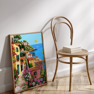 May include: A framed painting of a colorful Italian village with a blue ocean in the background. The painting is in a wooden frame and is leaning against a white wall.