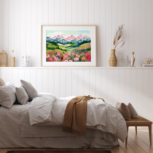 May include: A framed print of a colorful landscape painting with a mountain range in the background and a field of flowers in the foreground. The painting is in a light wood frame and is hanging on a white wall.