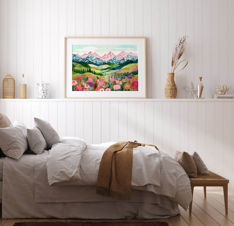 May include: A framed print of a colorful landscape painting with a mountain range in the background and a field of flowers in the foreground. The painting is in a light wood frame and is hanging on a white wall.