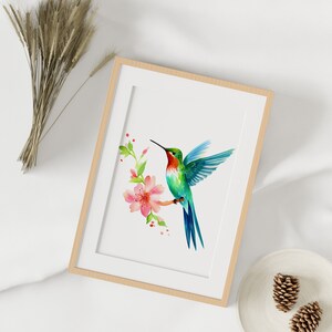 Puede incluir: Una pintura de acuarela enmarcada de un colibr&iacute; con plumas verdes y azules, flotando cerca de una flor rosa con hojas verdes. El fondo es blanco.