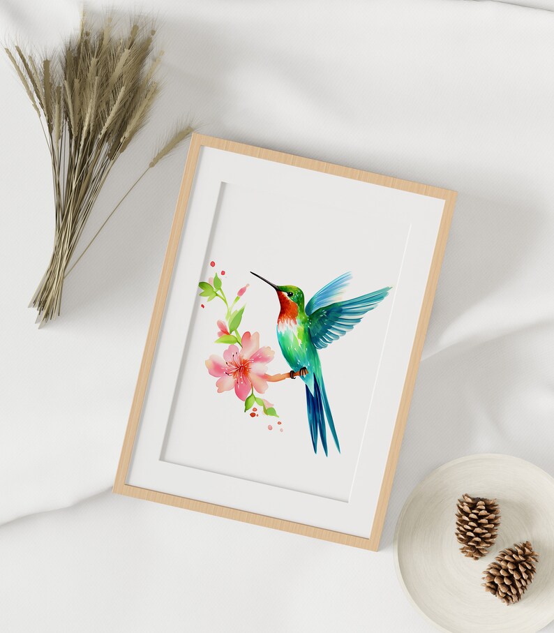Puede incluir: Una pintura de acuarela enmarcada de un colibr&iacute; con plumas verdes y azules, flotando cerca de una flor rosa con hojas verdes. El fondo es blanco.