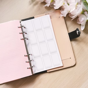 Puede incluir: Una agenda rosa y beige con un inserto de página blanco que presenta una cuadrícula de nueve cuadrados en blanco con cinco estrellas en la parte inferior de cada cuadrado.