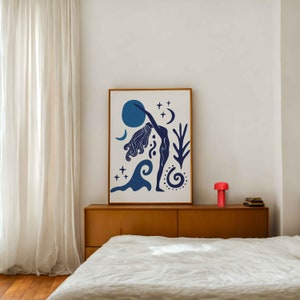Puede incluir: Una ilustración enmarcada de una mujer en una postura de yoga con formas abstractas azules y blancas y estrellas. La ilustración está sobre un fondo blanco y está enmarcada en un marco de madera claro.