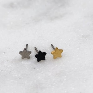 Puede incluir: Tres pequeños pendientes en forma de estrella en plata, negro y oro.