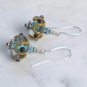 May include: A pair of dangle earrings with clear glass beads, yellow and brown accents, and turquoise and grey stones. The earrings have silver hooks.