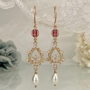 以下が含まれることがあります： 赤い四角い石、真珠のドロップ、繊細な花のデザインが施されたゴールドのドロップイヤリング