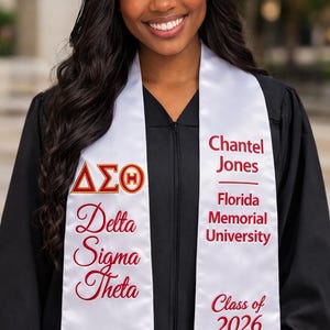 May include: A graduate in a black cap and gown, wearing a white sash. The sash displays the Delta Sigma Theta sorority letters, the name "Chantel Jones", and "Florida Memorial University" in red text. The class year "2026" is also shown.