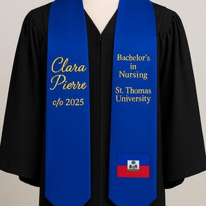 Op de afbeelding: Een blauwe afstudeer stropdas met gouden letters. Op de stropdas staat aan de ene kant "Clara Pierre c/o 2025" en aan de andere kant "Bachelor's in Nursing St. Thomas University". Onderaan is een Haïtiaanse vlag geborduurd.