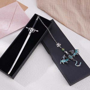 May include: Two black velvet boxes with silver sword and green dragon bookmarks. The sword bookmark has a silver handle and a black blade. The dragon bookmark has green and silver wings and a silver chain.