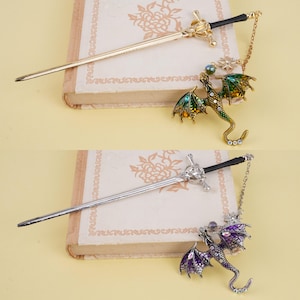 May include: Two gold and silver hair sticks with dragon charms. The sticks are sword-shaped and have black handles. The dragons are green and purple with jeweled accents.