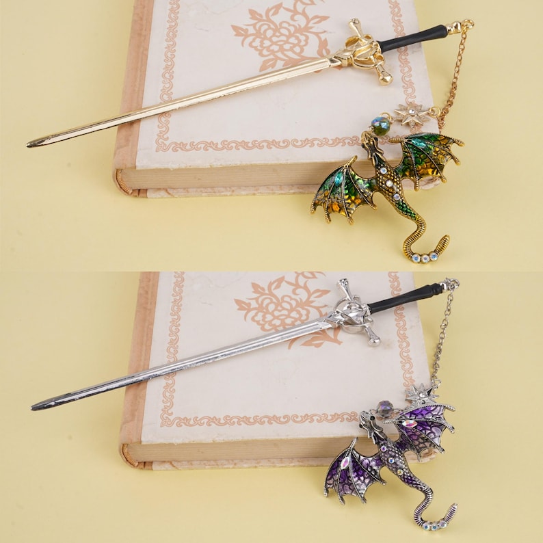 May include: Two gold and silver hair sticks with dragon charms. The sticks are sword-shaped and have black handles. The dragons are green and purple with jeweled accents.