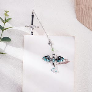 May include: Silver bookmark with a black sword and a blue and black dragon with green accents.