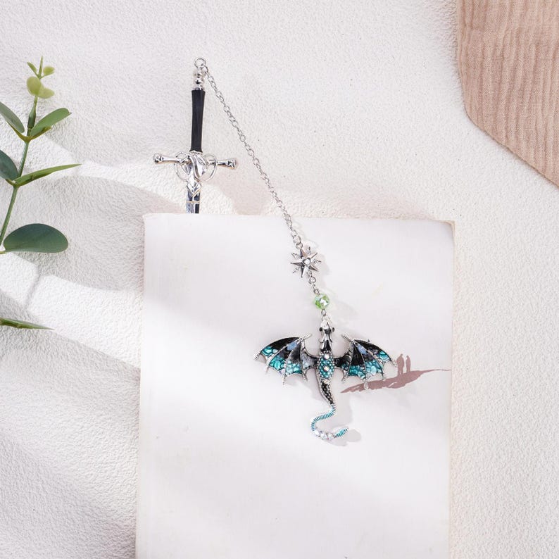 May include: Silver bookmark with a black sword and a blue and black dragon with green accents.