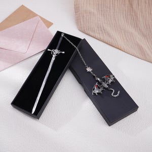 May include: A silver sword bookmark with a black handle and a dragon bookmark with red eyes and a silver chain.