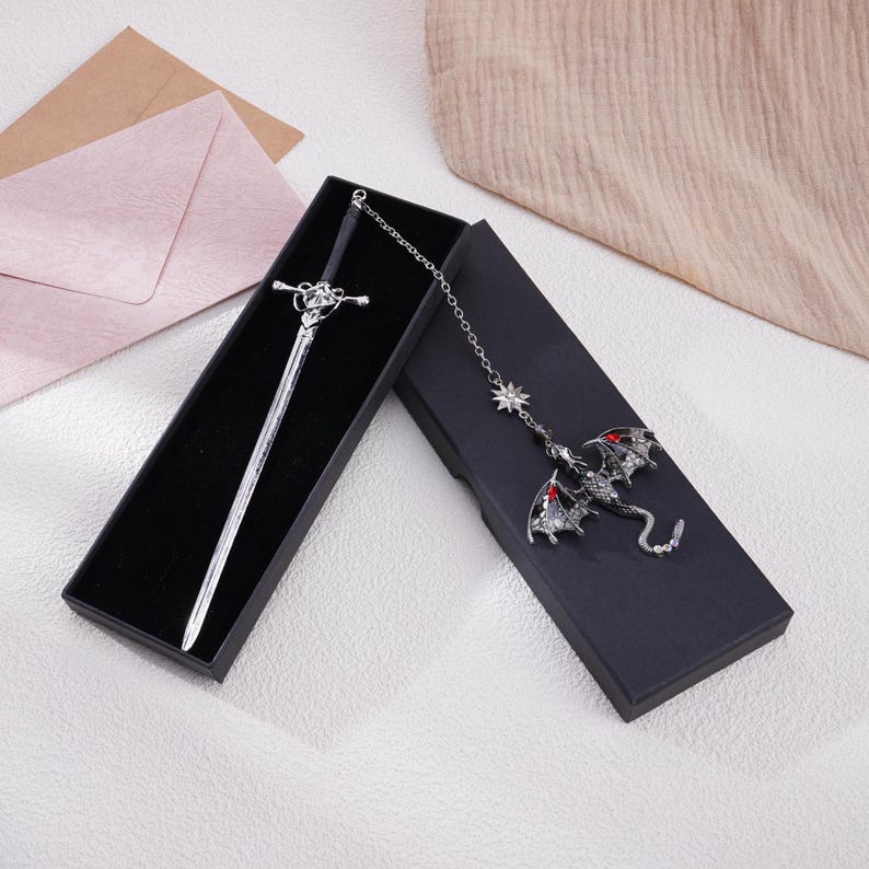 May include: A silver sword bookmark with a black handle and a dragon bookmark with red eyes and a silver chain.