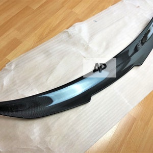 May include: A black carbon fibre rear spoiler for a car. The spoiler is curved and has a glossy finish.