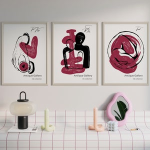 May include: Three framed abstract art prints with red and black ink drawings. The prints are titled "Antique Gallery" and have the text "Ink Collection" below the title. The prints are hanging on a white wall.