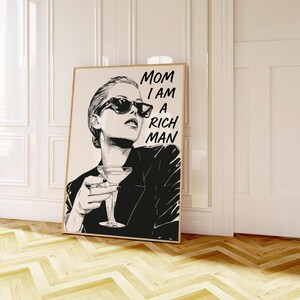 May include: Monochrome art print of a woman in sunglasses holding a cocktail, with the text "MOM I AM A RICH MAN". The artwork is displayed in a room with a wooden floor. The print is in a wooden frame.