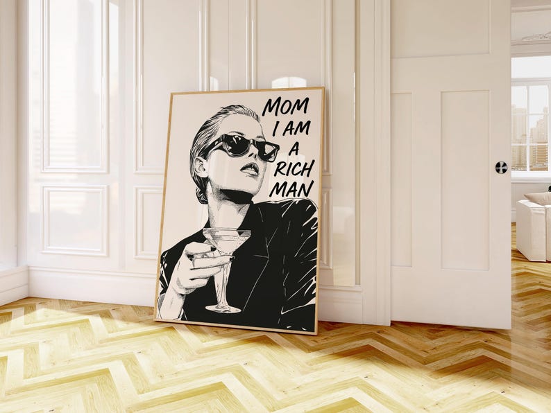 May include: Monochrome art print of a woman in sunglasses holding a cocktail, with the text "MOM I AM A RICH MAN". The artwork is displayed in a room with a wooden floor. The print is in a wooden frame.