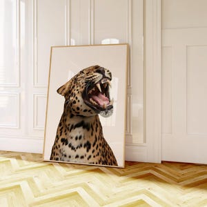 May include: A framed print of a roaring leopard, with its mouth wide open. The leopard's fur is tan with black spots. The artwork is displayed against a neutral background. The print is leaning against a white wall.
