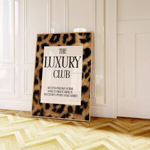 May include: A framed print with a leopard print border and the words "THE LUXURY CLUB" in bold black letters. The print also includes the text "SUCCESS FOLLOWS ACTION MAKE IT OWN IT GROW IT SUCCESSFUL PEOPLE MAKE MONEY."