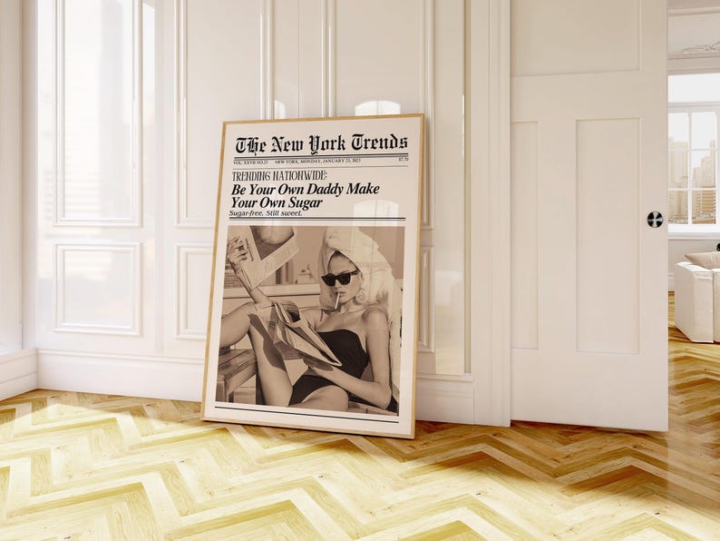 May include: A framed sepia-toned print of a newspaper titled "The New York Trends" with the headline "Be Your Own Daddy Make Your Own Sugar." The image within shows a woman in sunglasses and a towel, holding a newspaper.
