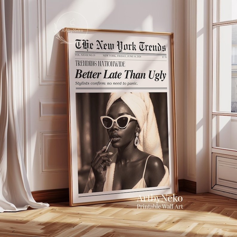 May include: A framed print featuring a sepia-toned image of a woman wearing sunglasses and applying lipstick. The print is designed to look like a newspaper, with the headline "Better Late Than Ugly" and "The New York Trends" at the top. The frame is gold.