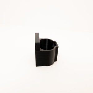 May include: A black plastic wall mount with a rounded opening, designed to hold a cylindrical object.