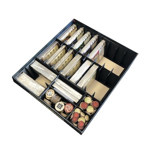 Puede incluir: Un organizador de juegos negro con múltiples compartimentos llenos de cartas de juego, fichas y otros componentes del juego. Las cartas son de varios tamaños y colores, y las fichas son redondas y coloridas. El organizador está diseñado para mantener las piezas del juego organizadas.