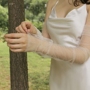 May include: A person wearing a white satin dress with sheer, white tulle elbow-length gloves.