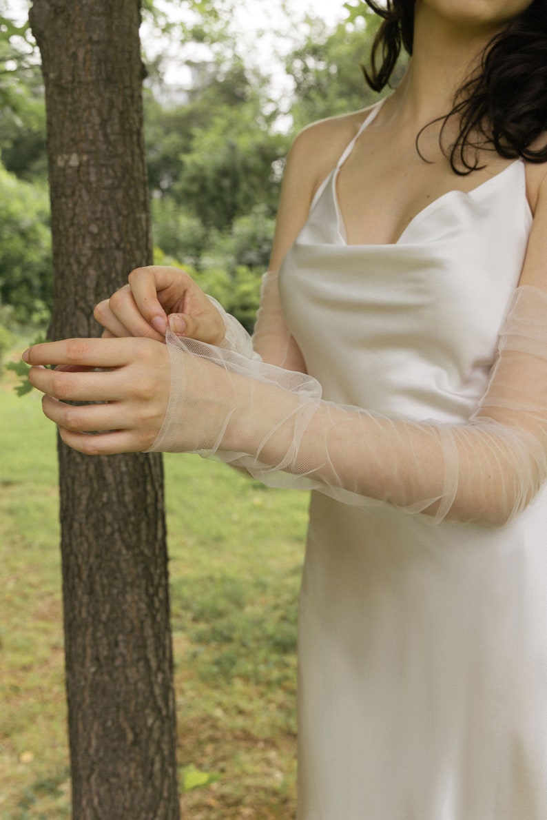 May include: A person wearing a white satin dress with sheer, white tulle elbow-length gloves.
