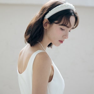 May include: A woman wearing a white sleeveless dress with a pearl necklace and a white headband with pearl embellishments.